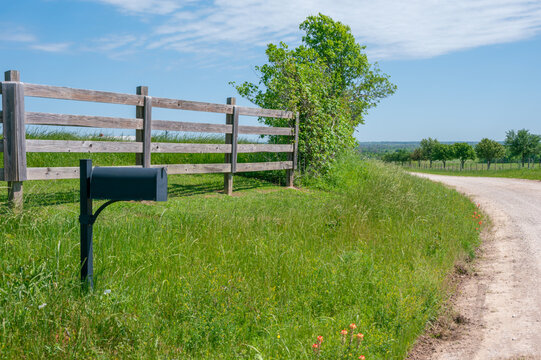 A mailbox and wooden fence on the side of a gravel road.