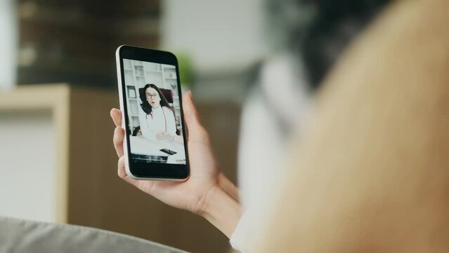 Close up of smartphone screen in patient's hand with young doctor therapist giving consultation advise by online video call conference meeting indoors Distance remote aid