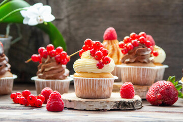 Chocolate and vanilla cupcakes decorated with fresh berries on rustic wooden background