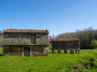 Fototapeta na wymiar Dos hórreos de piedra de distintos tamaños en un campo de hierba. Zas, A Coruña, España.