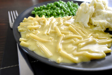 Macaroni and cheese with mashed potatoes and green peas on a plate.
