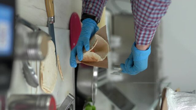 Vertical video of cook preparing Greek pita souvlaki sandwich with tzatziki sauce and fresh vegetables
