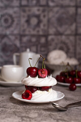 Mini Pavlova desserts with whipped cream and fresh cherries on a gray background. Meringue with berries. Light summer desserts.