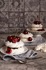 Mini Pavlova desserts with whipped cream and fresh cherries on a gray background. Meringue with berries. Light summer desserts.