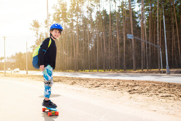happy child schoolboy with a backpack goes to school on a skateboard. a joyful boy with protection...