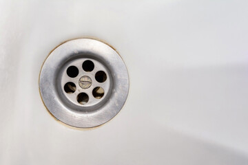 An old rusty bathtub with a metal drain hole. Dirty cracked unclean surface of the bath or sink with rust stain and lime deposits, close-up. Corrosion, unsanitary concept