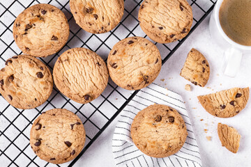 Close-up of baked oatmeal cookies with chocolate chips on a metal cooling rack and coffee in a white porcelain mug. Selective focus.
