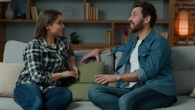 Caucasian couple sit on couch in living room carefree talk share news excited boyfriend talking to girlfriend tell story funny joke woman listen emotional man laughing dialogue conversation at home
