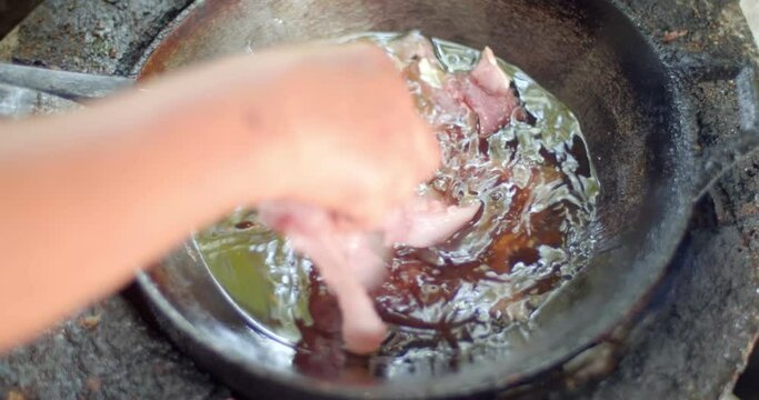 Clouse up hand 
putting pork in a frying pan with oil.Close-up of fried pork in old pan and hot oil from top view.One sun-dried pork in Thailand is popular to cook and eat.