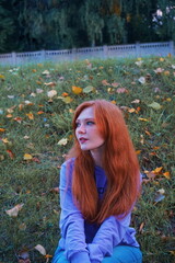 red haired girl sits on the grass near the fallen leaves