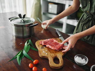 A woman in the kitchen prepares a dinner of meat and vegetables and spices on a wooden table against the backdrop of a stylish kitchen, close-up hands, fresh eco products, healthy nutrition, lifestyle