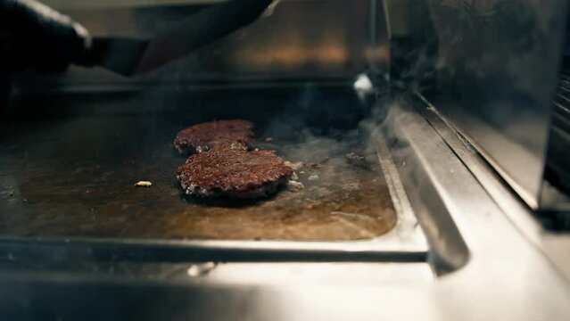 Professional restaurant kitchen close-up chef flips delicious juicy patties on grill with spatula for smash burger
