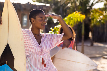 Happy diverse female friends holding surfboards at beach