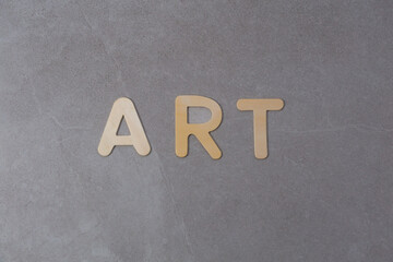 Blond wood capital letters spelling the word ART against textured grey tile