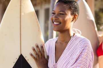 Happy african american woman holding surfboard at beach