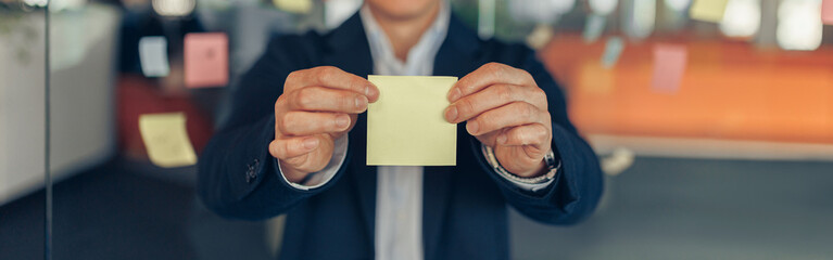Asian Businessman showing empty sticky notes while standing in modern office