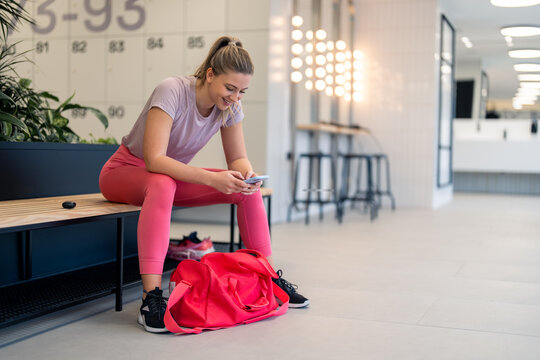 Happy satisfied young sports woman using smartphone and fitness mobile app at locker room in gym fitness center, tracking body wellness training progress after workout, practicing healthy lifestyle. - Powered by Adobe