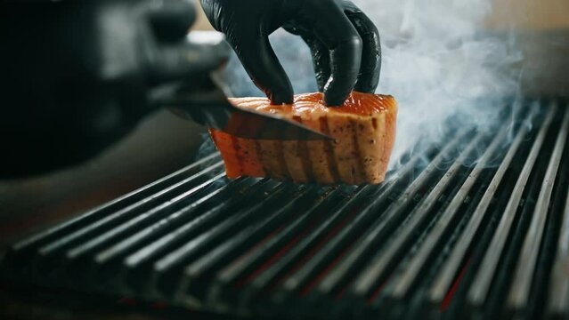 Professional kitchen in hotel restaurant close-up chef flips juicy piece of fresh grilled salmon texture of dish