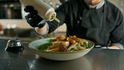 Professional kitchen in the restaurant of the hotel, the chef pours a spicy sauce on the seafood salad