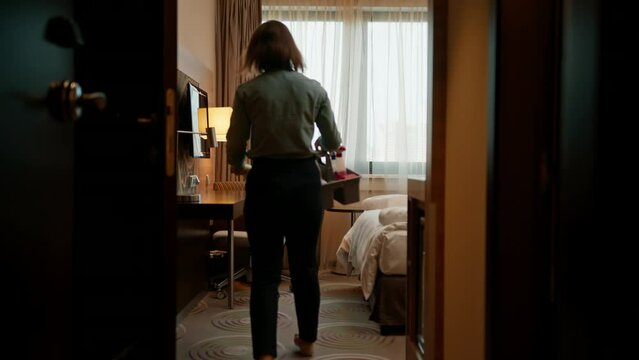 Housekeeper in uniform dusting while preparing luxury hotel room for guests cleaning and traveling concept