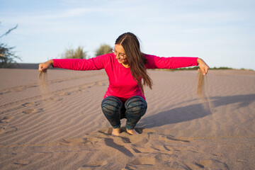 Latina brunette woman smiling and playing with her hands to release sand from the dunes of a south american beach