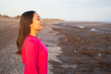 Latina and brunette woman breathing and feeling the nature of a marine beach rocks and dunes.