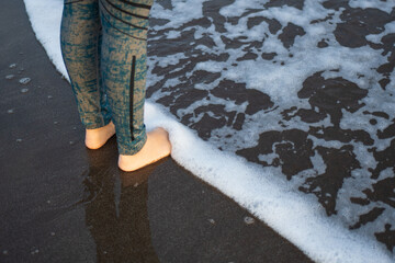 Feet of a brunette latina woman touching the foam and water of the sea.