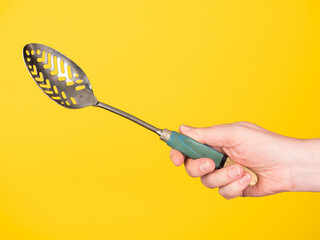 A hand holds an old skimmer. No face, yellow background, copy space.
