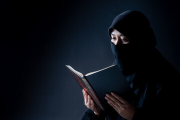 Portrait Asian Muslim woman standing and reading the Quran and appreciating and faith The Holy Al Quran with written Arabic calligraphy meaning of Al Quran, Arabic word translation: The Holy Al Quran.