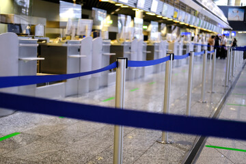 lobby of airport, blue barrier tape separates check-in counters for a flight without people,...