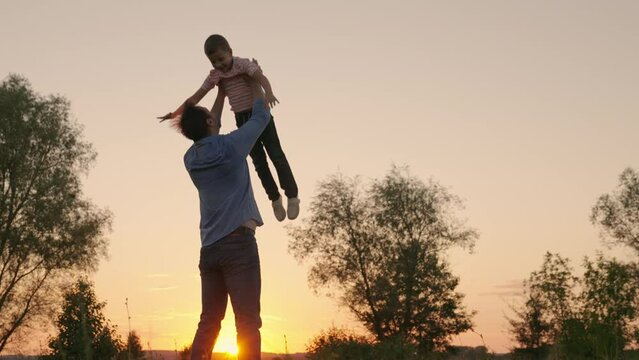 Family game concept, Child, superhero, fly. Dad plays with his son, throws up child with his hands in sky, outdoors. Happy Father, child, little boy have fun together in park, sun. Kid fatherhood