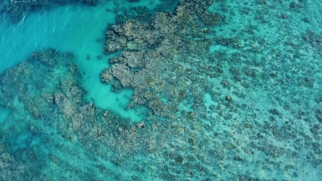 Aerial drone shot flying slowly over reef with clear blue ocean and waves crashing on reef in Western Australia