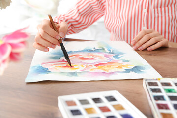 Woman painting flowers with watercolor at wooden table, closeup. Creative artwork