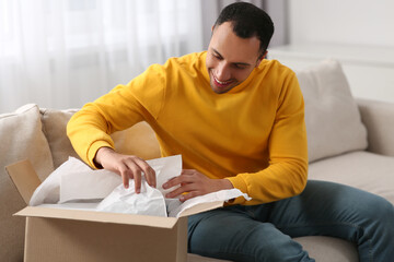 Fototapeta premium Happy young man opening parcel at home. Internet shopping
