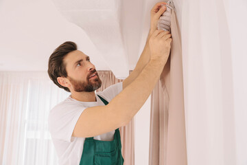 Worker in uniform hanging window curtain indoors