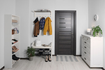 Beautiful hallway interior with coat rack, chest of drawers and shoe storage bench near wooden door