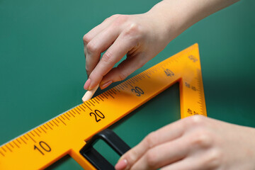 Woman drawing with chalk and triangle ruler on green board, closeup