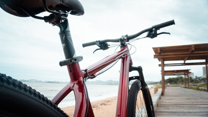 Fototapeta na wymiar Bicicleta vermelha apoiada na beira da praia em dia claro
