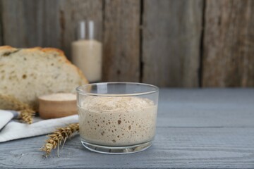 Glass jar with sourdough on grey wooden table. Space for text