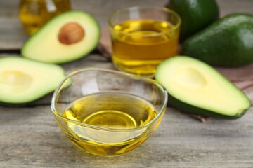 Bowl with oil and ripe fresh avocados on wooden table, closeup