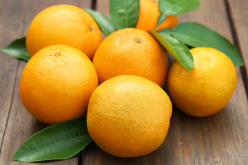 Many ripe oranges and green leaves on wooden table, closeup