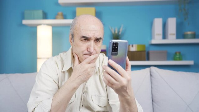 The old man using the phone gets sad and emotional.
Elderly man feeling emotional and saddened by an image or a message on a smartphone at home.
