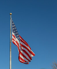 Close up view of an American flag waving on a flagpole, with blue sky background and copy space
