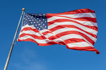 Close up view of an American flag waving on a flagpole, with blue sky background and copy space
