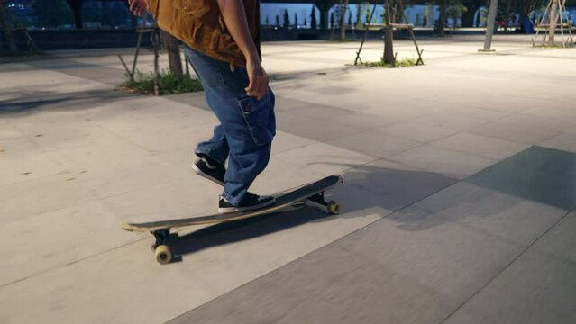 4K Cool Asian guy skating on longboard skate at public park on summer holiday vacation. Handsome man enjoy and fun urban active lifestyle practicing outdoor sport skateboarding on city street at night