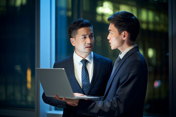 two asian businessmen discussing business in office using laptop computer