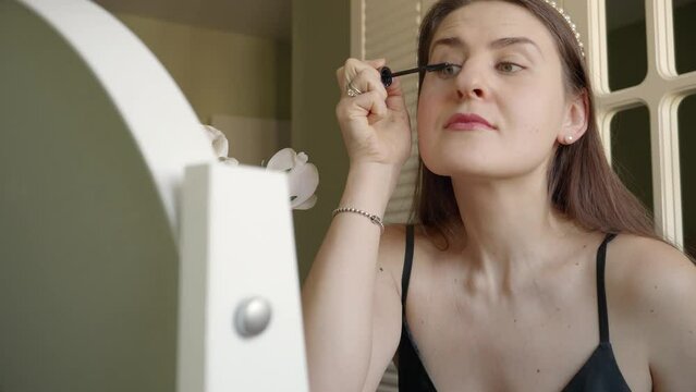 Portrait of elegant woman applying mascara at bedroom makeup table. Skin care, female health and beauty