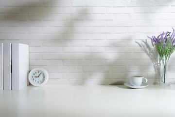 Minimal workplace with books, clock and coffee cup on white table against brick wall.