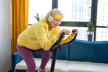 elderly caucasian woman training and doing exercise on cycle at home. active pensioner lifestyle...