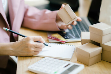 Asian Women business owner working at home with check online orders to prepare to pack the boxes, sell to customers, sme business ideas online.
